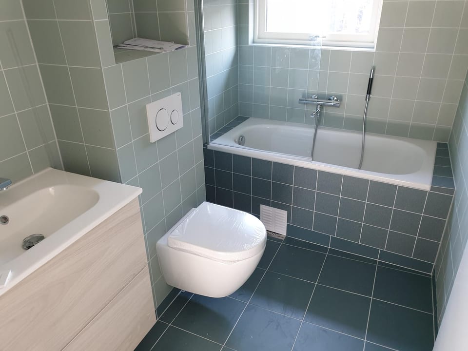 Flislagt bad med badekar og vegghengt toalett